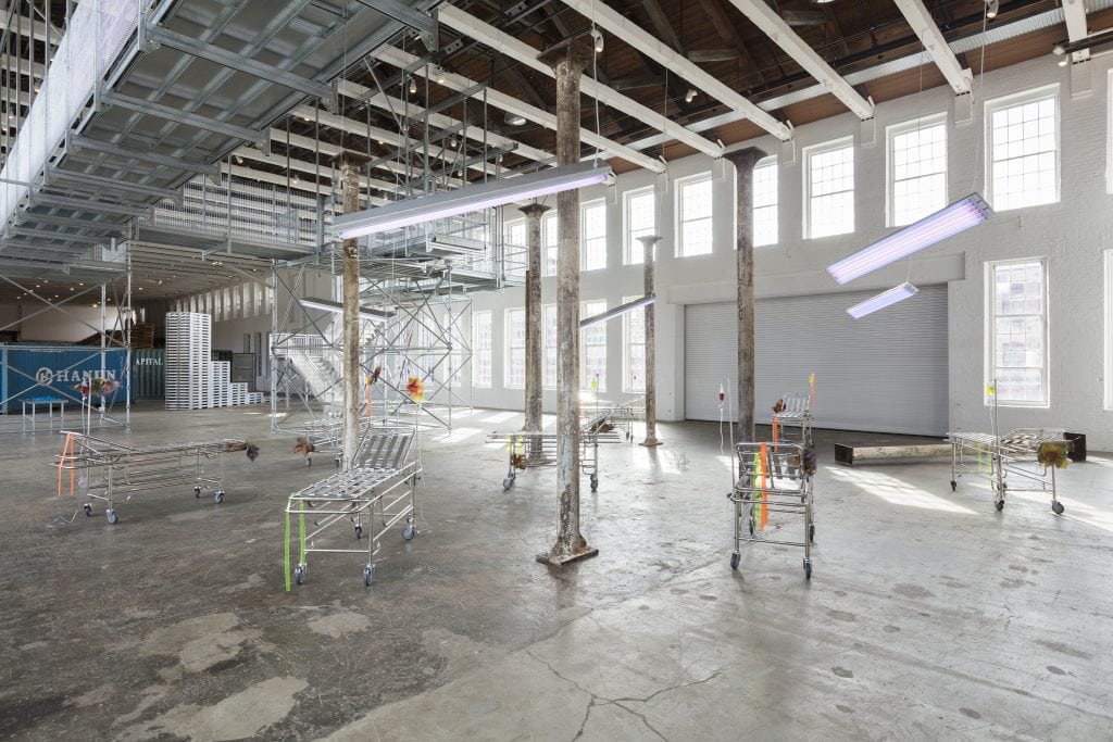 Liz Glynn "Post-industrial Vacationland (After Aldous Huxley)," 2017 Reclaimed cast-iron columns, selections from the “Neverwork“ series (modified stainless steel gurneys and aqua-resin) and the “Desert Future” series (cast stainless steel tumbleweeds), and tanning lamps, dimensions variable