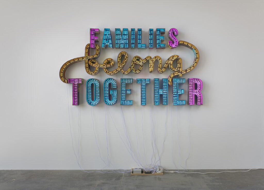 This image depicts an artwork by Andrea Bowers titled "Families Belong Together." This artwork was created in 2018 and measures 9' 1 ⁷⁄₈" x 58 ¹³⁄₁₆" [HxW] (279.12 x 149.35 cm). Its medium is Cardboard, LED lights.