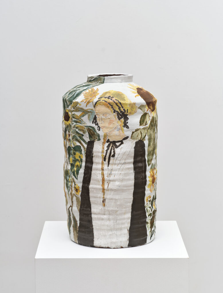 This image depicts an artwork by Shanna Waddell titled "Sheness Stands Amongst Sunflowers." This artwork was created in 2025 and measures 18 ¹⁄₂" x 11" x 11" [HxWxD] (46.99 x 27.94 x 27.94 cm). Its medium is Ceramic, Underglaze.